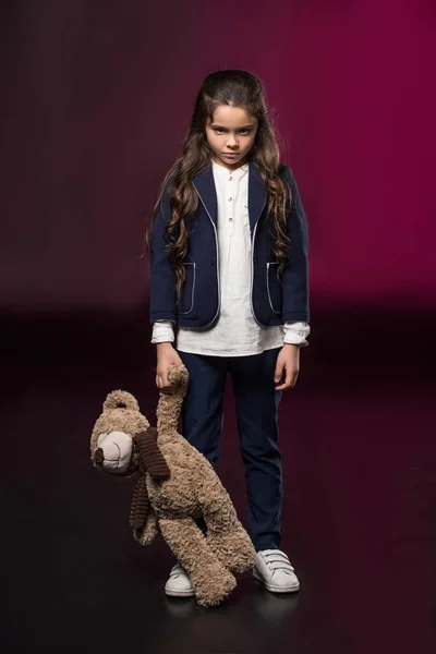 Arrabbiato bambino in piedi e tenendo orsacchiotto su bordeaux — Foto stock