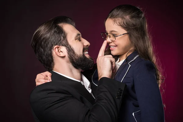 Father touching daughter nose with finger on burgundy — Stock Photo