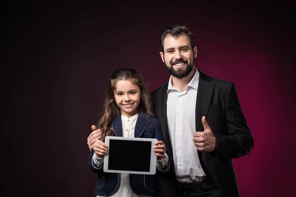 Daughter holding tablet and father showing thumb up on burgundy — Stock Photo