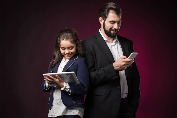 Отец и дочь с помощью планшета и смартфона на бордовом — стоковое фото