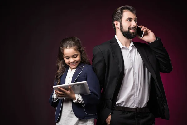 Daughter using tablet and father talking by smartphone on burgundy — Stock Photo