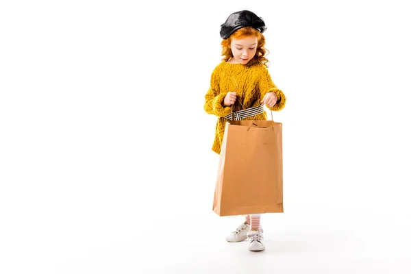 Felice bambino capelli rossi in cerca di shopping bag isolato su bianco — Foto stock