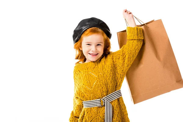 Sonriente pelo rojo niño sosteniendo bolsa de compras en mano aislada en blanco - foto de stock
