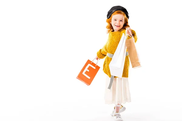 Niño pelo rojo feliz mostrando bolsas de compras aisladas en blanco - foto de stock
