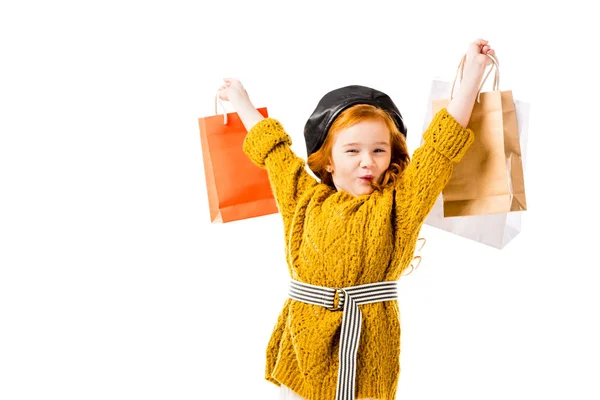 Criança cabelo vermelho feliz segurando sacos de compras em mãos acima da cabeça isolado no branco — Fotografia de Stock