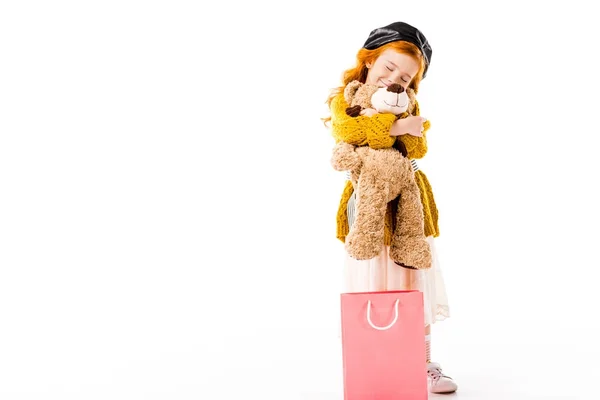 Enfant roux souriant étreignant ours en peluche avec les yeux fermés isolé sur blanc — Photo de stock