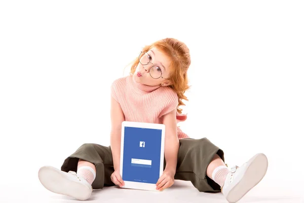 Rotes Haar Kind sitzt und hält Tablet mit geladener Facebook-Seite auf weiß — Stockfoto