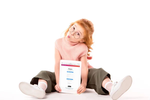 Red hair child sitting and holding tablet with loaded instagram page on white — Stock Photo