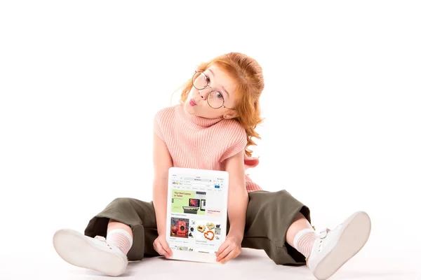 Рыжий ребенок сидит и держит планшет с загруженной страницы Ebay на белом — стоковое фото