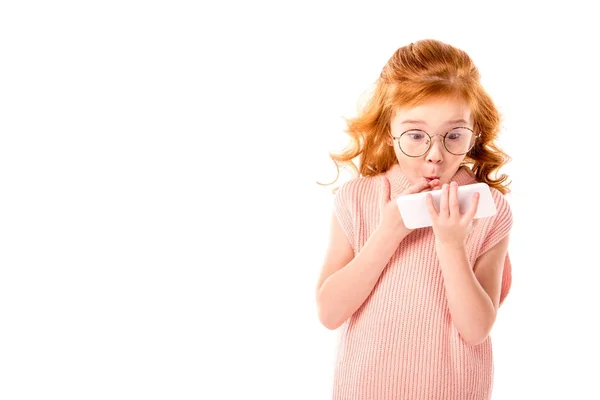 Surprised kid with ginger hair looking at smartphone isolated on white — Stock Photo