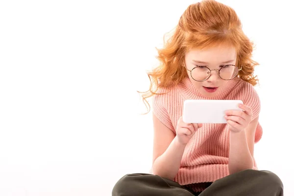 Surprised redhead kid looking at smartphone isolated on white — Stock Photo