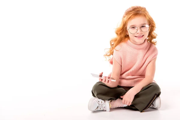 Kid with ginger hair sitting and holding smartphone on white — Stock Photo