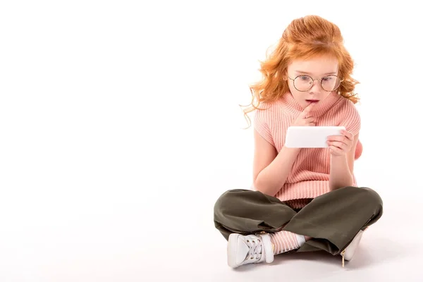 Rousse enfant regardant smartphone avec surprise sur blanc — Photo de stock