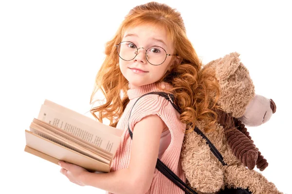 Criança cabelo vermelho de pé com livro e ursinho isolado no branco — Fotografia de Stock