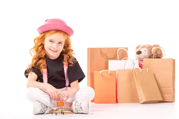 Lächelndes Kind sitzt mit Einkaufswagen-Spielzeug auf weißem Grund — Stockfoto