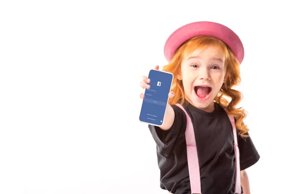 Niño con estilo en sombrero rosa y tirantes mostrando teléfono inteligente con página de Facebook aislado en blanco - foto de stock