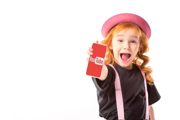 Elegante bambino in cappello rosa e bretelle mostrando smartphone con pagina youtube isolato su bianco — Foto stock