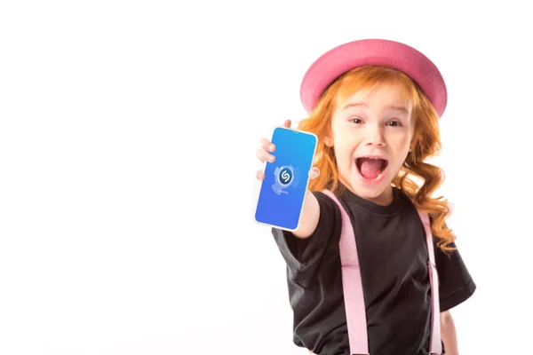 Élégant enfant en chapeau rose et bretelles montrant smartphone avec programme de musique isolé sur blanc — Photo de stock