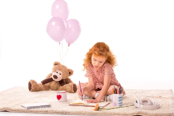 Kind sitzt auf Teppich und zeichnet in Notizbuch isoliert auf Weiß — Stockfoto
