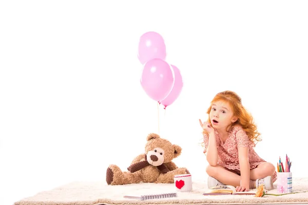 Sorprendido pelo rojo niño sentado con juguetes en la alfombra aislado en blanco - foto de stock