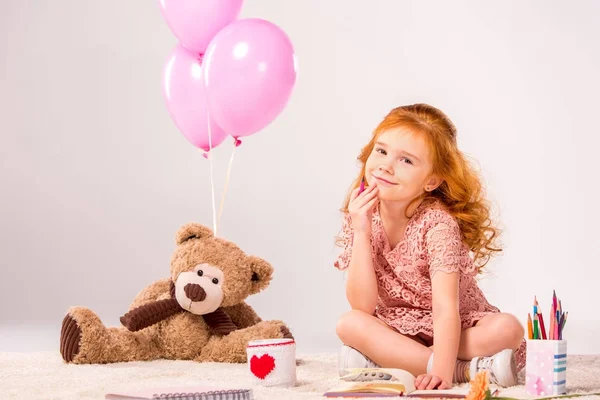 Руда дитина сидить на килимі з плюшевим ведмедем і повітряними кулями — стокове фото
