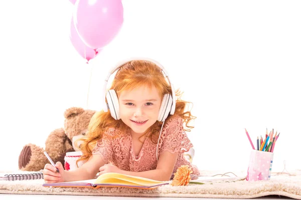Niño sonriente dibujando y escuchando música en alfombra aislada en blanco - foto de stock