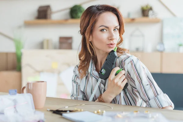 Fröhliche junge Frau hat Spaß mit Klebepistole in handgefertigter Werkstatt — Stockfoto
