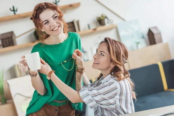 Happy young women trying on handmade accessory at workshop — Stock Photo