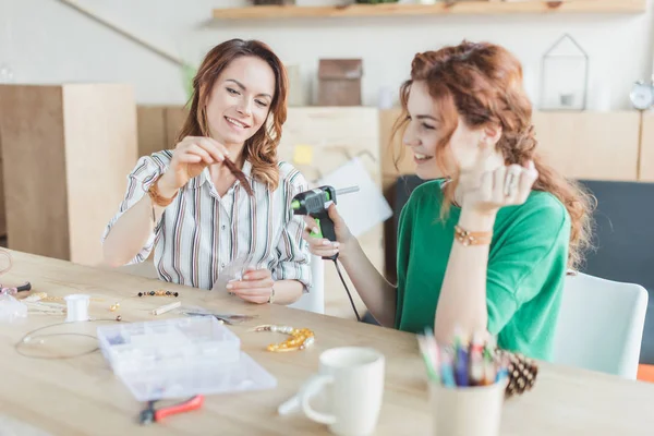 Mujeres jóvenes que trabajan con pistola de pegamento en taller de accesorios hechos a mano - foto de stock