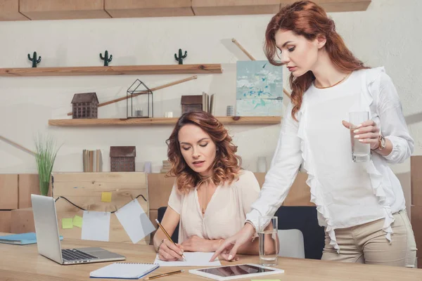 Young lady boss curating work of manageress while she writing — Stock Photo