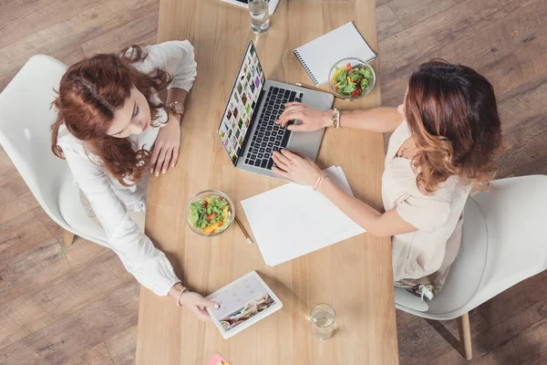Top view of buisnesswomen having lunch together and using laptop and tablet at office — Stock Photo