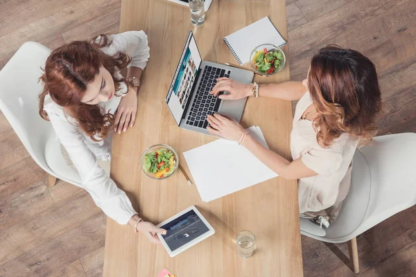 Blick von oben auf junge Geschäftsfrauen, die gemeinsam zu Mittag essen und Geräte im Büro benutzen — Stockfoto