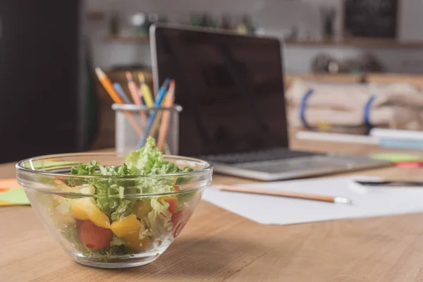 Plan rapproché du lieu de travail avec ordinateur portable et salade saine — Photo de stock