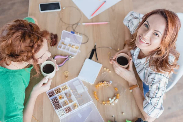 Vista de ángulo alto de las mujeres jóvenes felices beber café en taller de accesorios hechos a mano - foto de stock