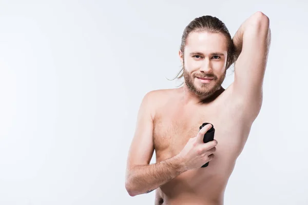 Smiling young man using deodorant spray with hand behind head, isolated on gray — Stock Photo