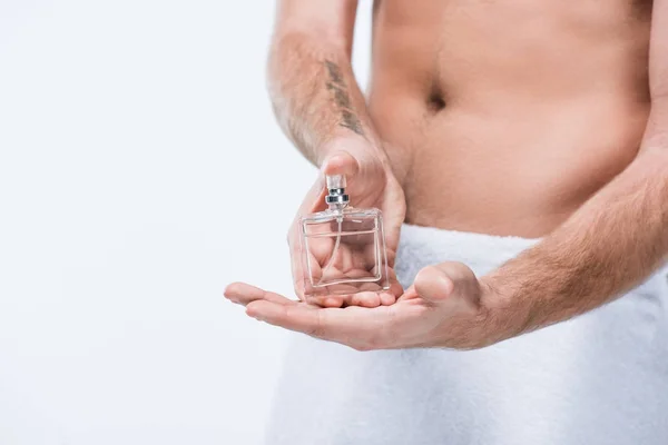 Image recadrée de l'homme avec une serviette autour de la taille tenant bouteille en verre avec du parfum, isolé sur blanc — Photo de stock