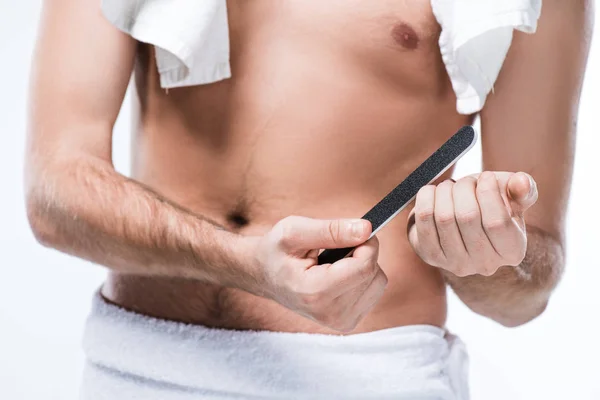 Sección media del hombre con toalla de baño en los hombros y alrededor de la cintura sosteniendo la lima de uñas en la mano, aislado en blanco - foto de stock