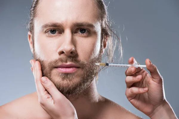 Caucasian brunette man looking at camera while persons hands making injection in his cheek, isolated on gray — Stock Photo