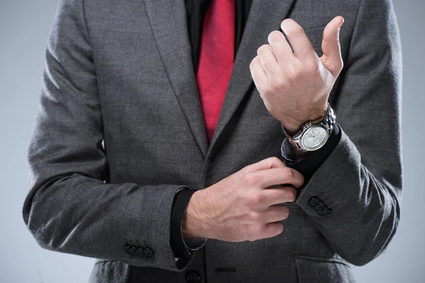 Midsection of businessman in formal suit adjusting button on sleeve, isolated on gray — Stock Photo