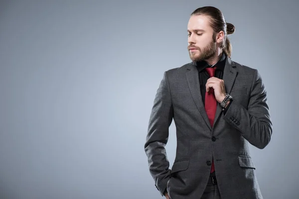 Молодий бізнесмен з закритими очима торкається його червоної краватки в той час як інша рука в кишені куртки, ізольовані на сірому — стокове фото