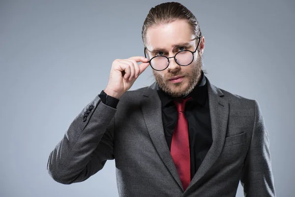 Nahaufnahme eines Geschäftsmannes im formellen Anzug, der im Stehen seine Brille berührt, isoliert auf grau — Stockfoto