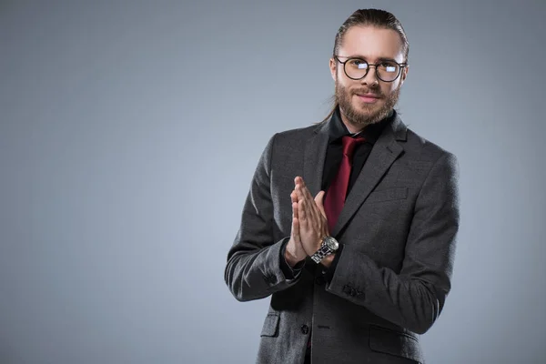 Young businessman in glasses with folded hands smiling to camera, isolated on gray — Stock Photo