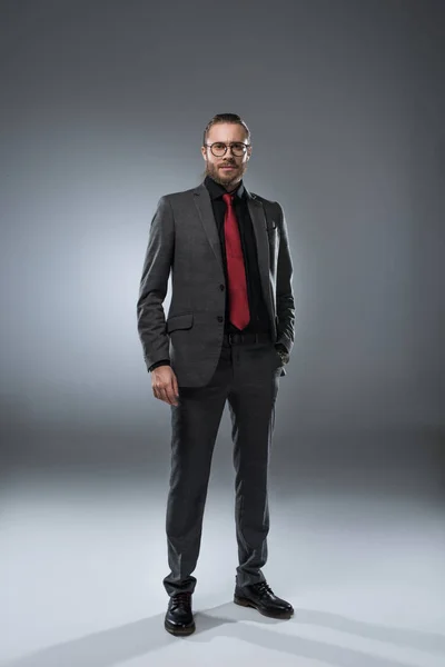 Uomo d'affari sieroso in occhiali in abito formale guardando la fotocamera, isolato su grigio — Foto stock