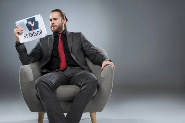 Homem de negócios barbudo caucasiano sentado em poltrona e lendo jornal, isolado em cinza — Fotografia de Stock