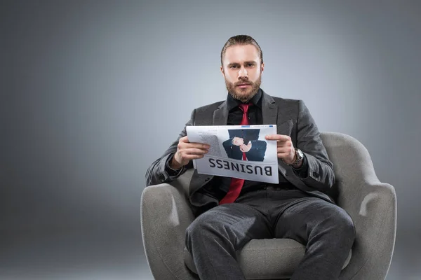 Kaukasischer bärtiger Geschäftsmann im Sessel sitzend und mit Zeitung in der Hand, während er in die Kamera blickt, isoliert auf grau — Stockfoto