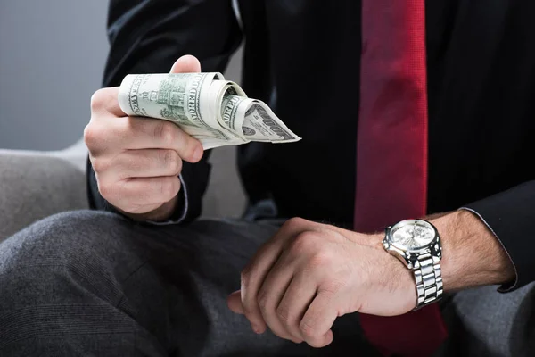 Midsection of businessman sitting in armchair  and holding money in hand, isolated on gray — Stock Photo