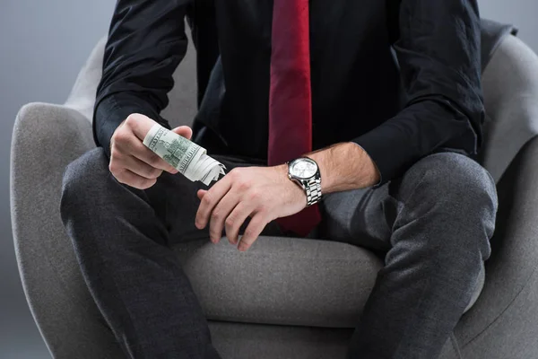 Sección media del hombre de negocios sosteniendo el dinero en las manos, mientras está sentado en el sillón, aislado en gris - foto de stock
