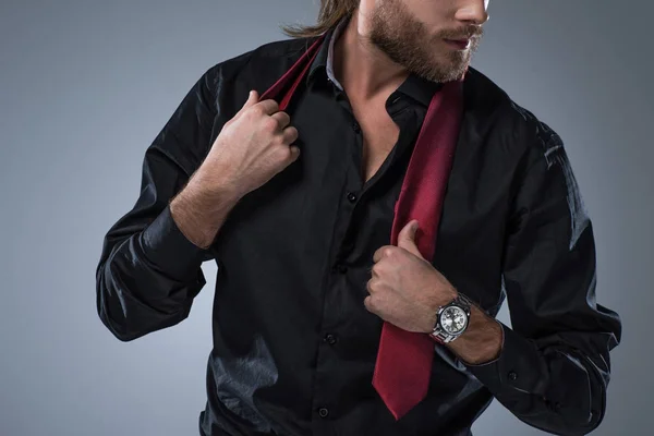 Imagen recortada de hombre barbudo en camisa negra con corbata roja alrededor de su cuello, aislado en gris — Stock Photo