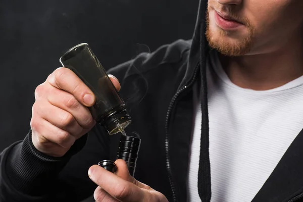 Vista recortada do homem enchendo cigarro eletrônico com e-líquido isolado em preto — Fotografia de Stock