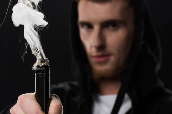 Молодой бородатый человек активирует электронную сигарету, изолированную на черном — стоковое фото